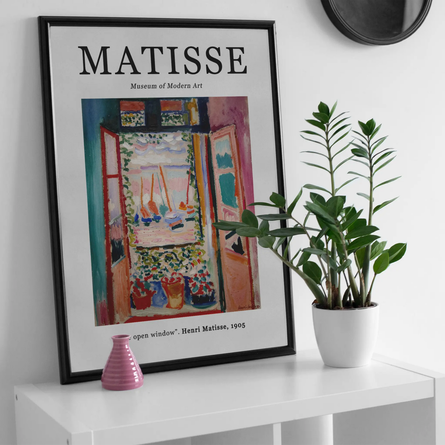 Framed Matisse artwork on a white wall with a plant and vase below.