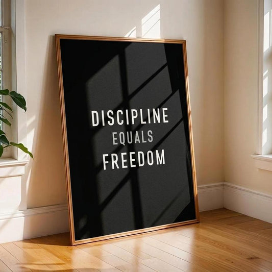 A framed motivational poster leaning against a wall in a sunlit room. The poster has a black background with the text 'DISCIPLINE EQUALS FREEDOM' in white, and a thin gold frame.