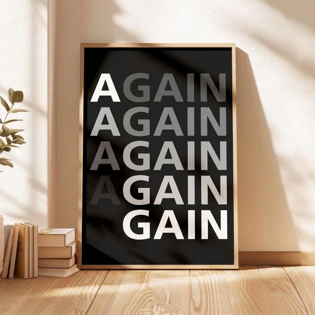 A framed typographic wall art print leaning against a beige wall on a wooden floor, with stacked books and a plant nearby. The print has a black background, large repeated text reading 'AGAIN AGAIN AGAIN AGAIN GAIN' in white and gray, and a light wood frame.
