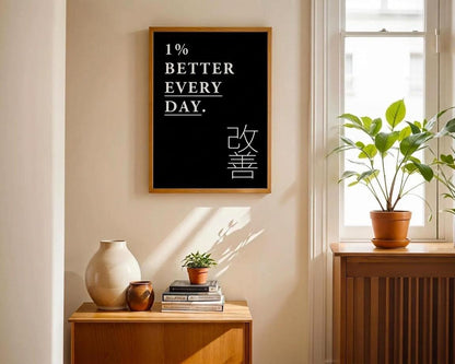 A framed black wall art print with the text '1% BETTER EVERY DAY.' and Japanese characters hangs on a beige wall in a sunlit room.