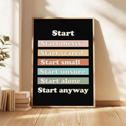 A framed motivational poster with a black background and colorful text blocks reading 'Start messy', 'Start scared', 'Start small', 'Start unsure', 'Start alone', and 'Start anyway', leaning against a beige wall on a wooden floor with sunlight and shadows.