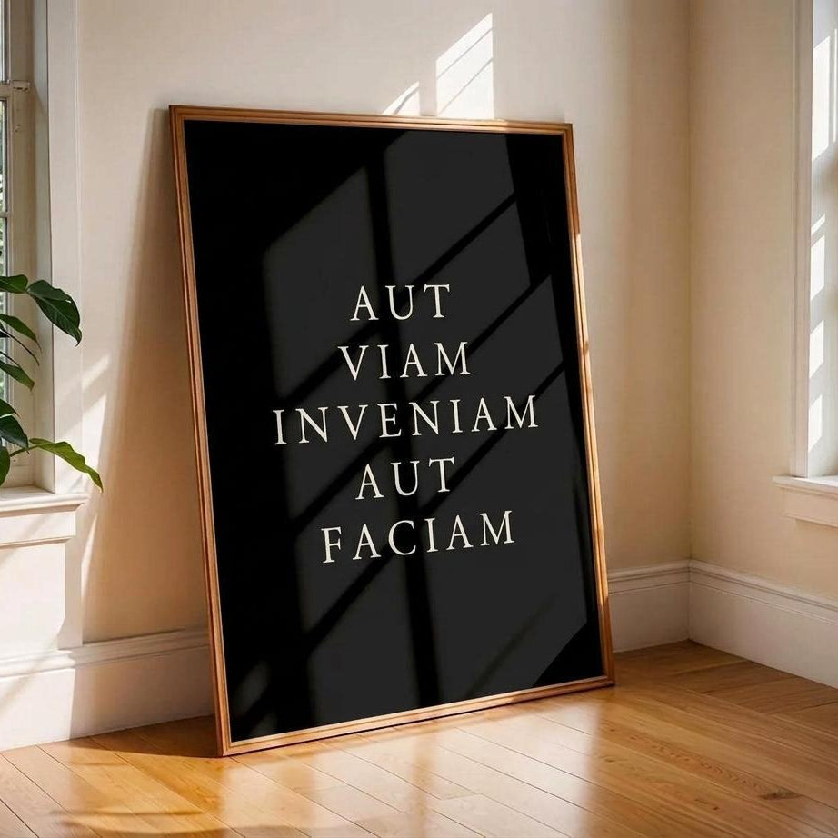 A vertical framed art print with a black background and white text reading 'MEMENTO MORI' and 'CARPE DIEM' leans against a cream-colored wall on a wooden floor in a sunlit room.