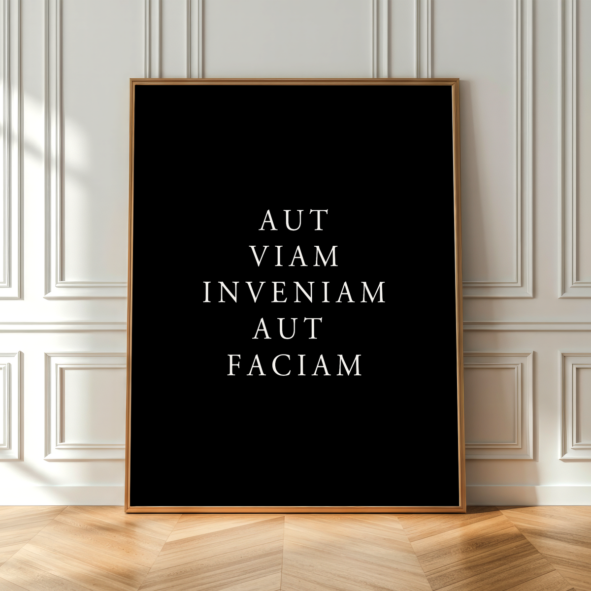 A vertical framed art print with the Latin phrase 'AMOR FATI CARPE DIEM' in white serif text on a black background, leaning against a white paneled wall on a light wood herringbone floor.