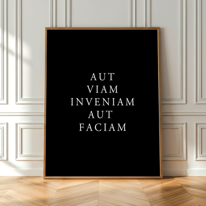 A vertical framed art print with the Latin phrase 'AMOR FATI CARPE DIEM' in white serif text on a black background, leaning against a white paneled wall on a light wood herringbone floor.