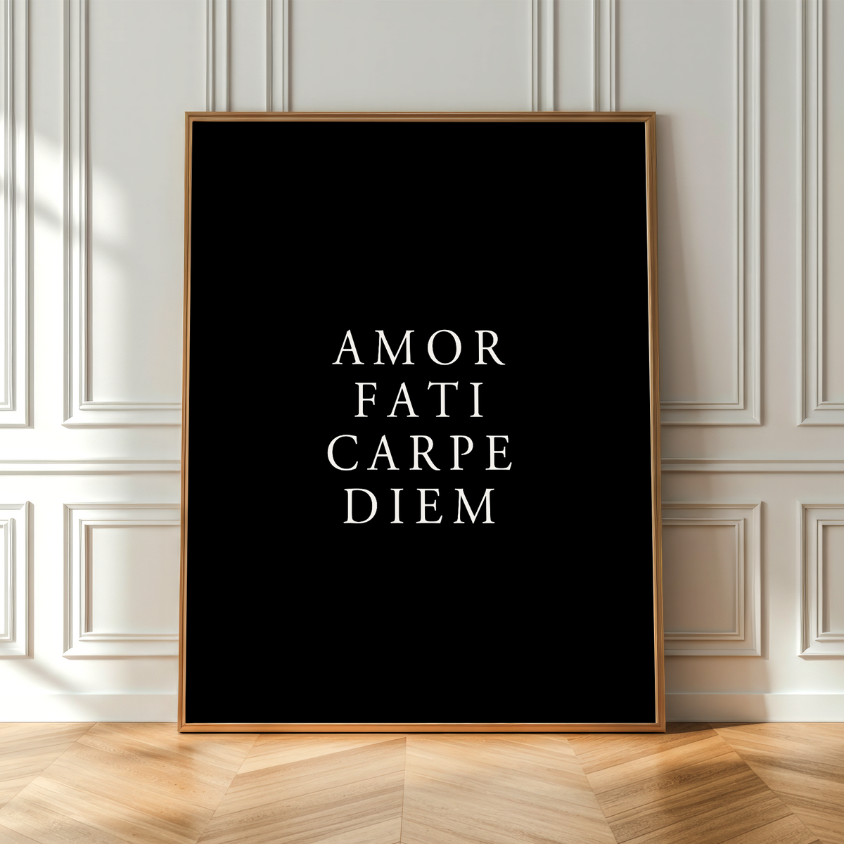 A vertical framed art print with the Latin phrase 'AMOR FATI CARPE DIEM' in white serif text on a black background, leaning against a white paneled wall on a light wood herringbone floor.