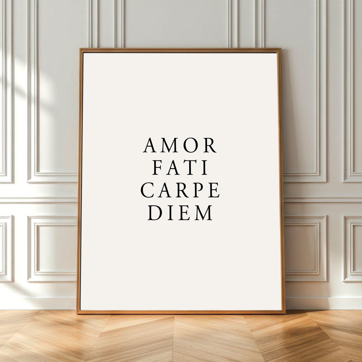 A vertical framed art print with the Latin phrase 'AMOR FATI CARPE DIEM' in black serif text on an off-white background, leaning against a light gray paneled wall on a light wood herringbone floor.
