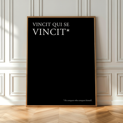 A vertical black poster with a thin gold frame leans against a white paneled wall on a light wood herringbone floor. The poster features the white text 'VINCIT QUI SE VINCIT*' at the top and a small footnote at the bottom reading '*He compares who compares himself.