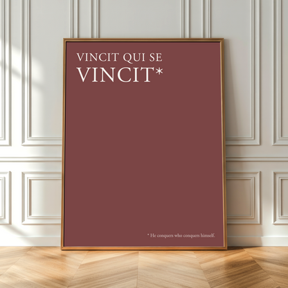 A framed minimalist art print with a terracotta red background and white text reading 'VINCIT QUI SE VINCIT*' leaning against a white paneled wall on a light wood herringbone floor.
