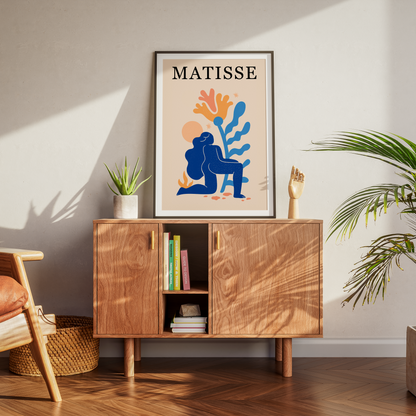 A framed Matisse art print with a colorful blue, orange, and beige illustration hangs on a light gray wall above a mid-century modern wooden sideboard.