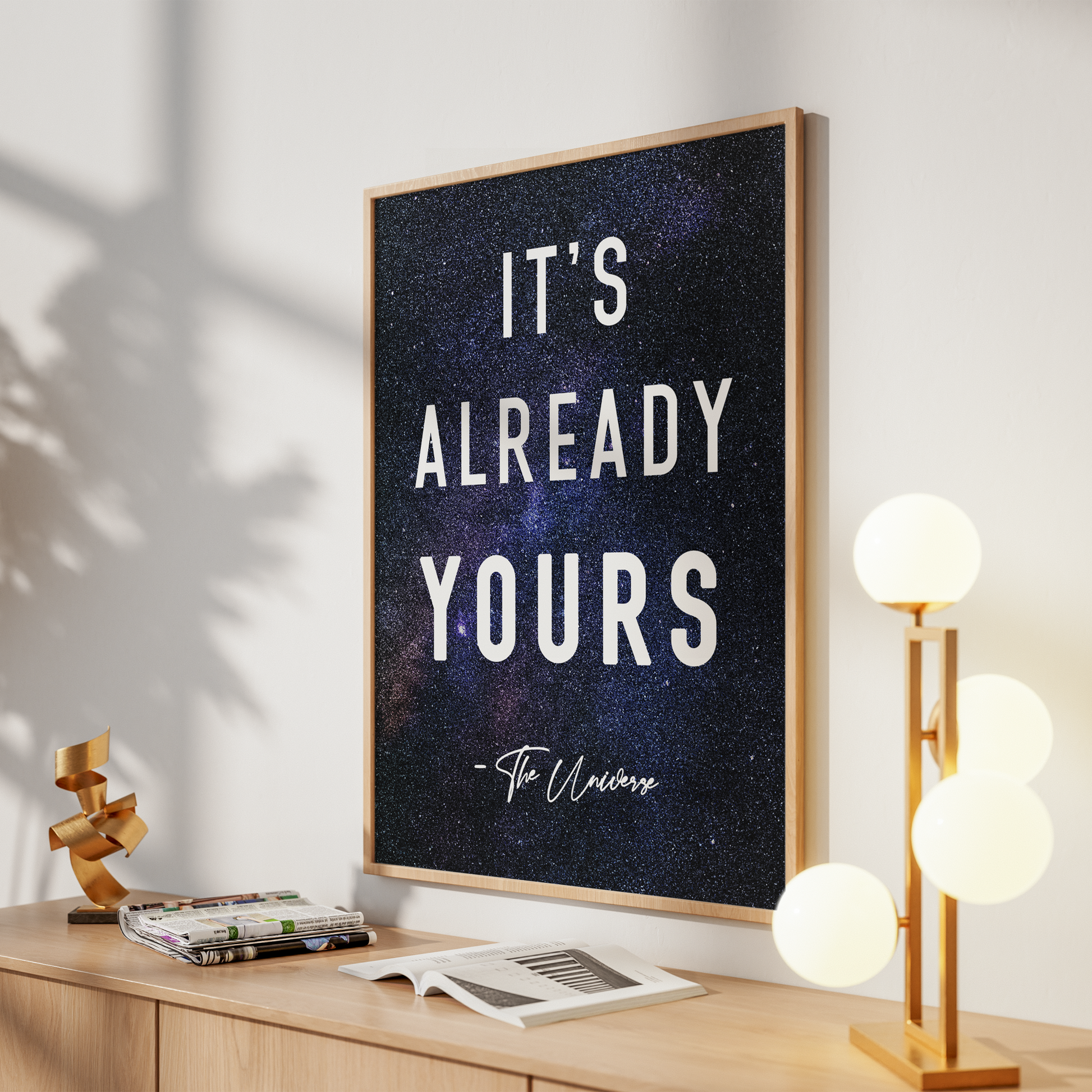 A framed wall art print with the quote 'IT'S ALREADY YOURS - The Universe' in white text over a dark starry cosmic background