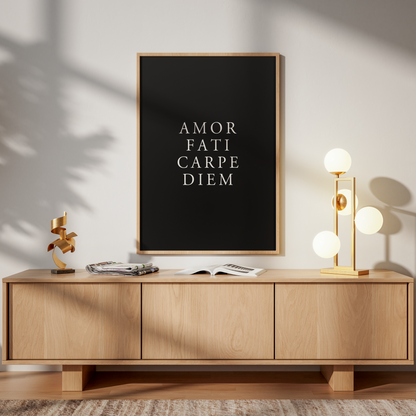 A framed black poster with white text reading 'AMOR FATI CARPE DIEM' hangs above a light wood sideboard in a styled interior. The room has warm sunlight shadows, a gold floor lamp, books, and a wooden chair.