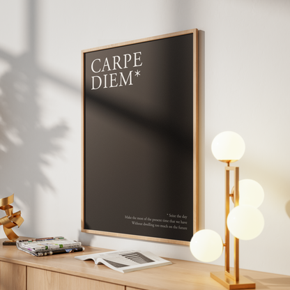 A framed wall art print with the text 'CARPE DIEM*' on a dark background, leaning on a light wood console table in a styled interior with a glowing multi-light lamp and soft shadows.