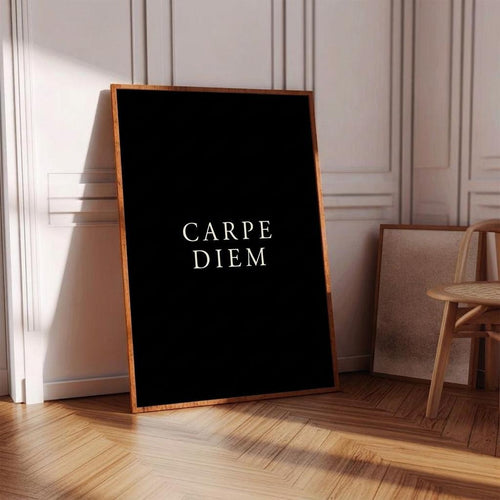 A framed black art print with the Latin phrase 'CARPE DIEM' in white serif text, leaning against a white paneled wall on a wooden floor in a sunlit room.
