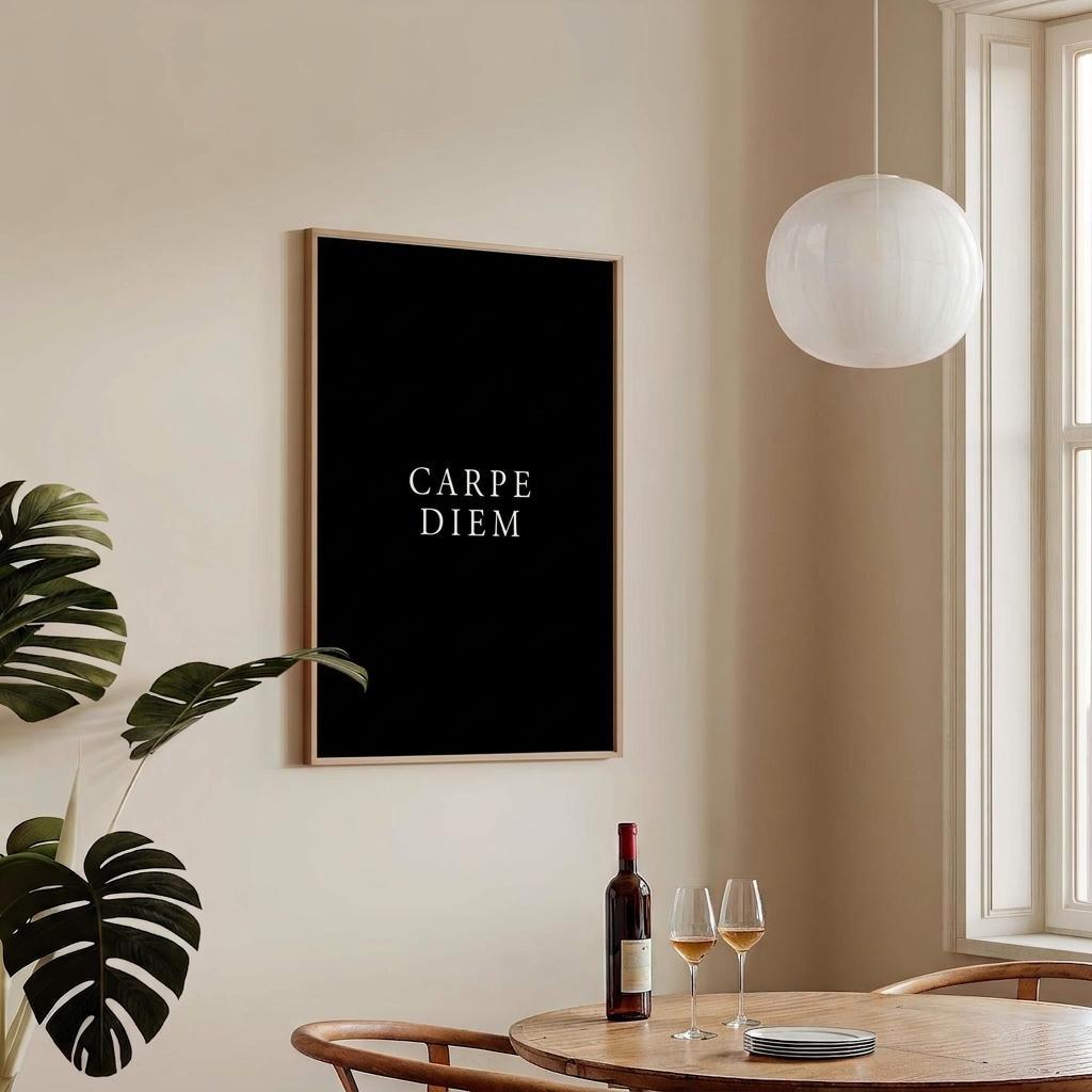 A framed black wall art print with the words 'CARPE DIEM' in white serif text hangs on a beige wall in a bright dining room. A wooden table with two wine glasses and a bottle, a white pendant light, and a window are visible.