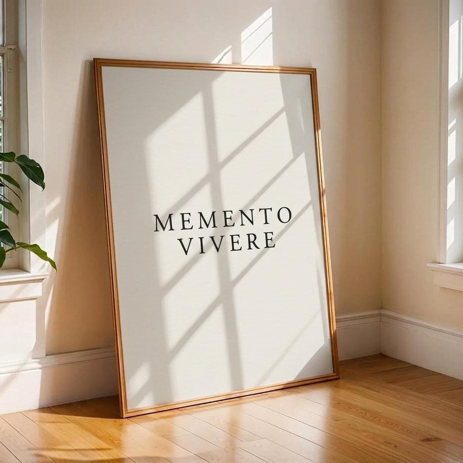 A framed minimalist art print with the text 'MEMENTO VIVERE' in black serif letters on a white background, leaning against a beige wall on a wooden floor in a sunlit room.