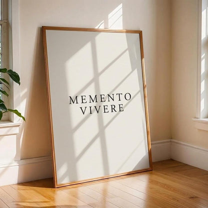 A framed minimalist art print with the text 'MEMENTO VIVERE' in black serif letters on a white background, leaning against a beige wall on a wooden floor in a sunlit room.