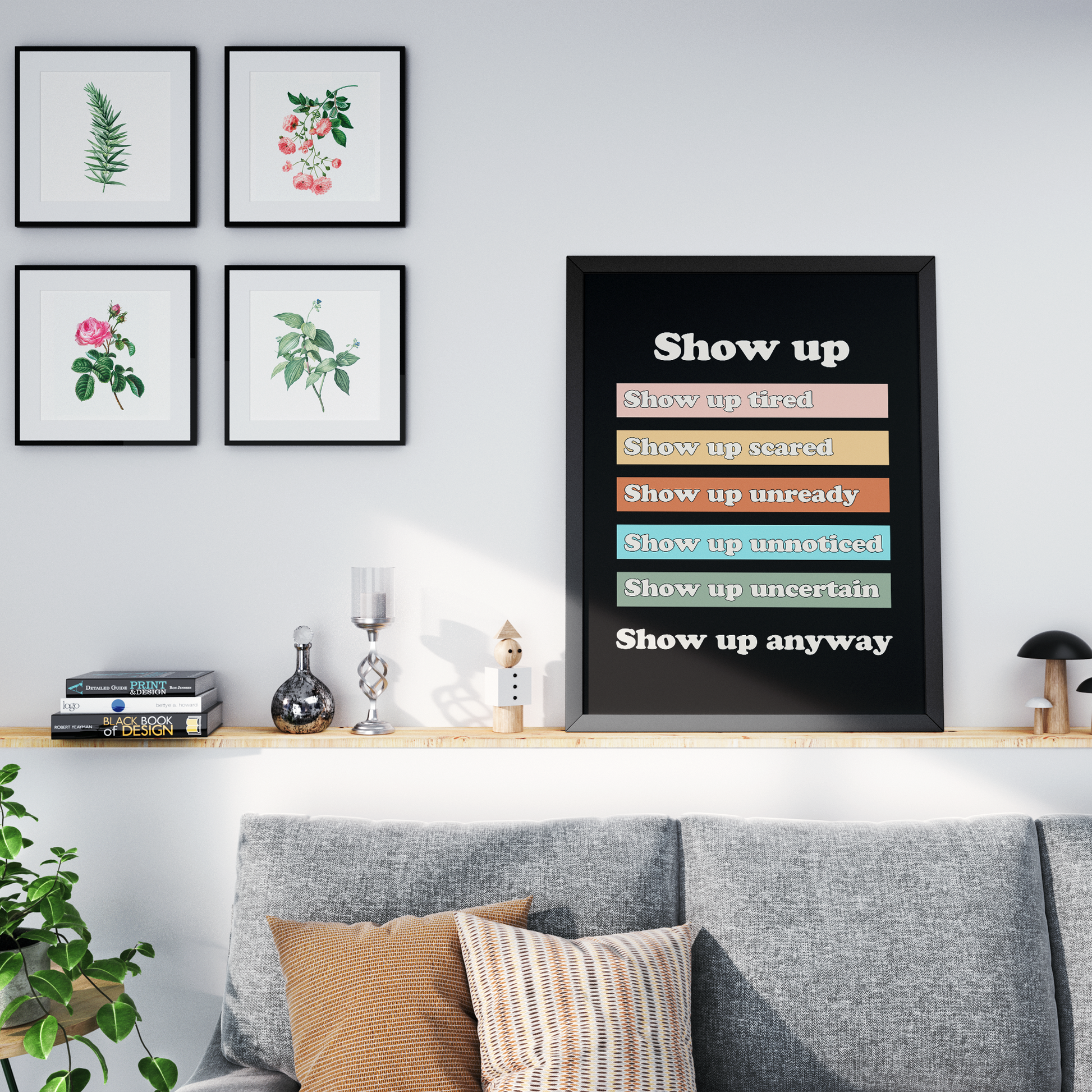 A framed motivational wall art print with the text 'Show up' in stacked color-coded status rows, displayed on a shelf in a styled living room setting above a gray sofa.