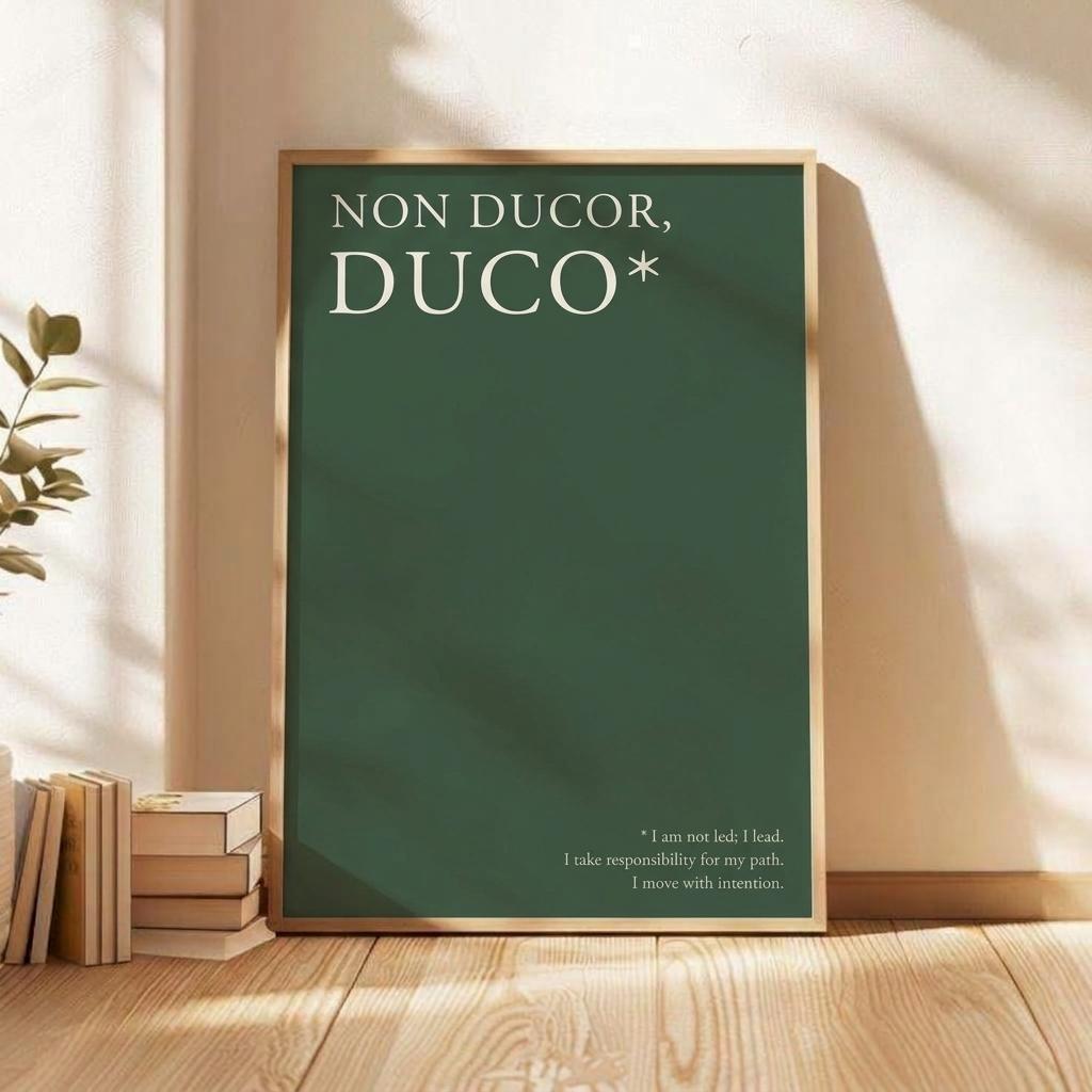 A framed art print featuring the Latin phrase 'NON DUCOR, DUCO*' in white text on a dark green background, styled leaning against a beige wall on a wooden floor next to books.