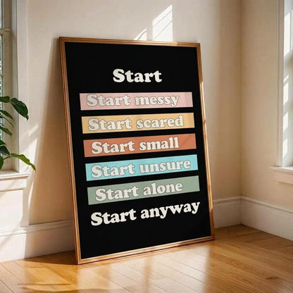 A framed motivational poster leaning against a beige wall on a wooden floor in a sunlit room. The poster has a black background with white text reading 'Start' followed by stacked pastel phrases: 'Start messy', 'Start scared', 'Start small', 'Start unsure', 'Start alone', and 'Start anyway'.