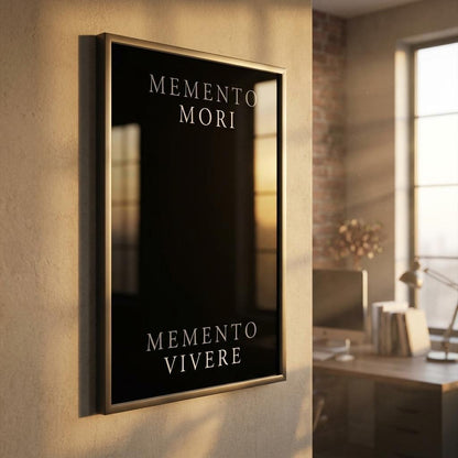A vertical framed wall art print with a black background and gold-toned border, mounted on a beige wall in a modern office setting. The print features the Latin phrases 'MEMENTO MORI' at the top and 'MEMENTO VIVERE' at the bottom in white serif text.