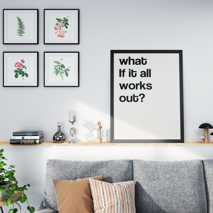 A framed typographic wall art print reading 'what if it all works out?' displayed in a styled living room above a gray sofa, next to four smaller botanical art prints on a white wall.