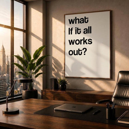 A framed motivational wall art print with the text 'what if it all works out?' hanging in a modern, sunlit office setting with a desk, chair, and city view.
